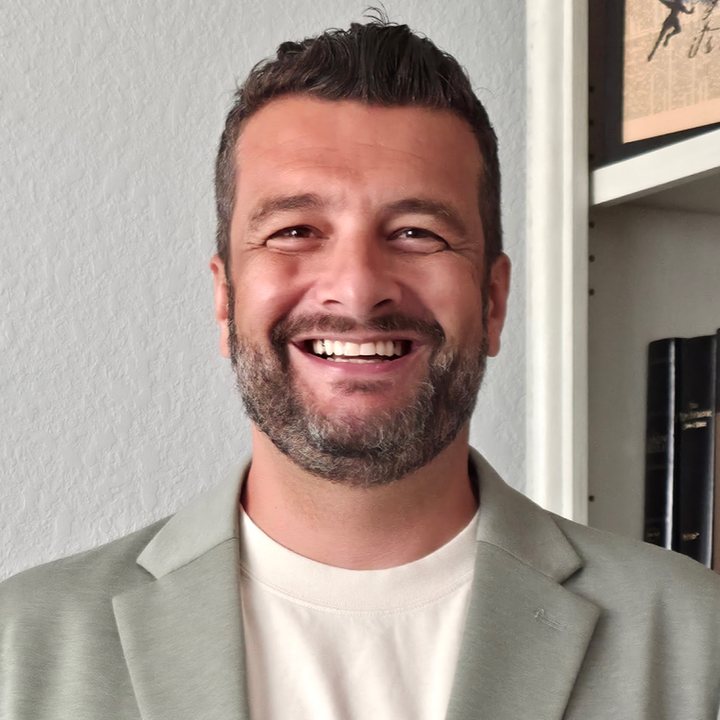 Jay, smiling, in a gray jacket in front of a bookshelf.